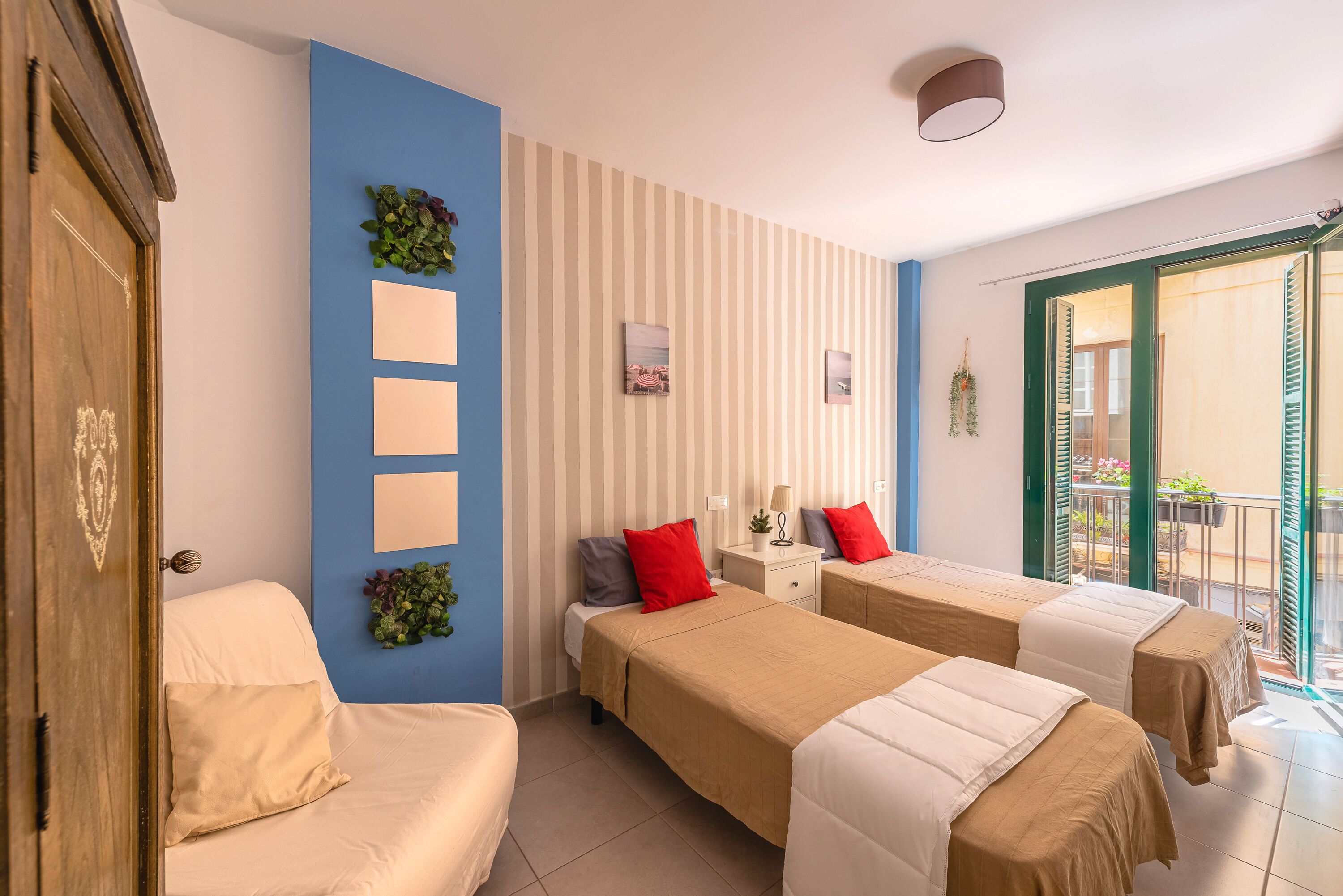 A hotel room with two beds, a small bedside table, a wall-mounted plant, and a sliding glass door to the balcony.