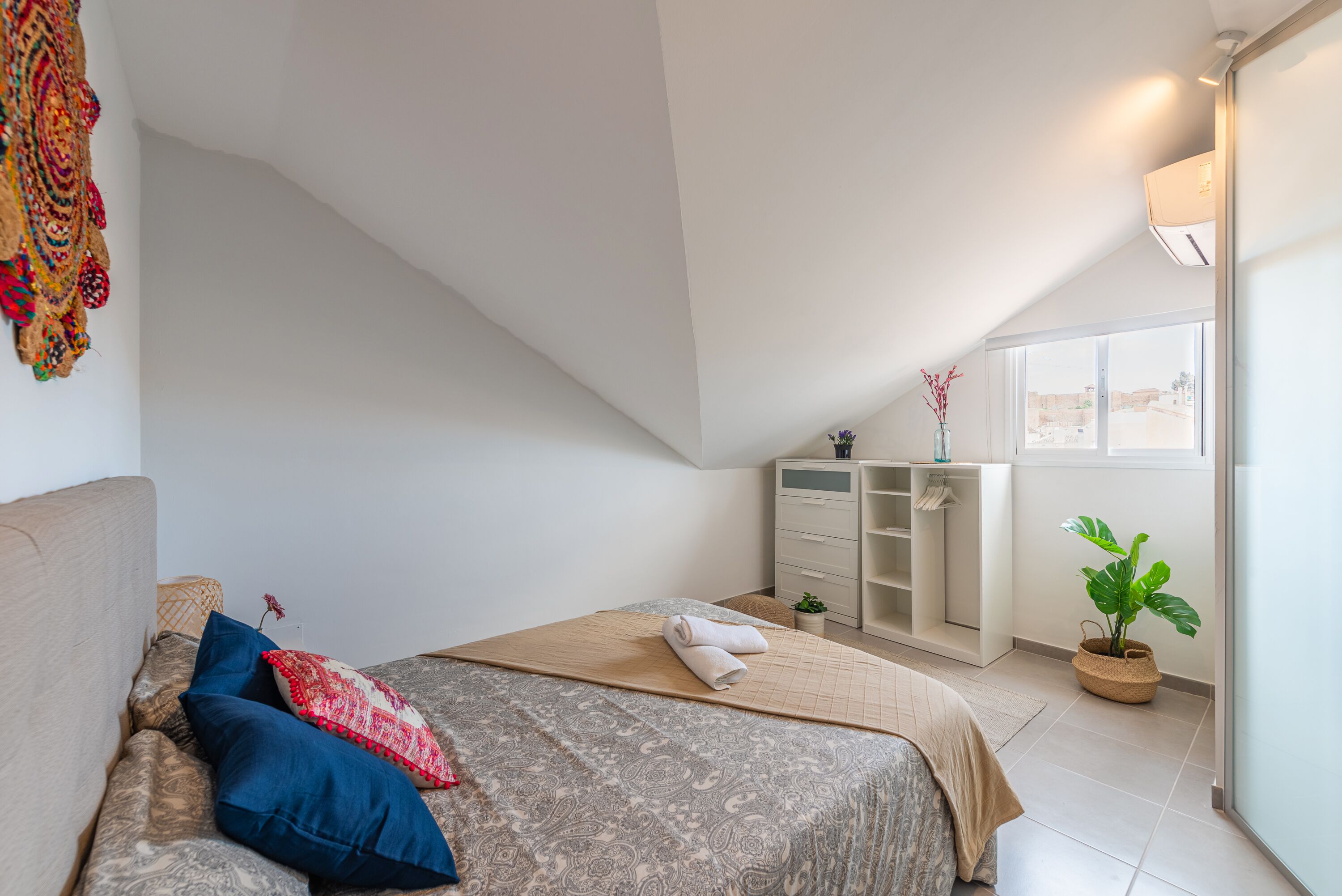 A bedroom with a bed, a dresser, a potted plant, and a window.
