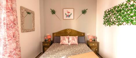 Un dormitorio ordenado con una cama, dos mesitas de noche, un espejo y una planta en la pared.