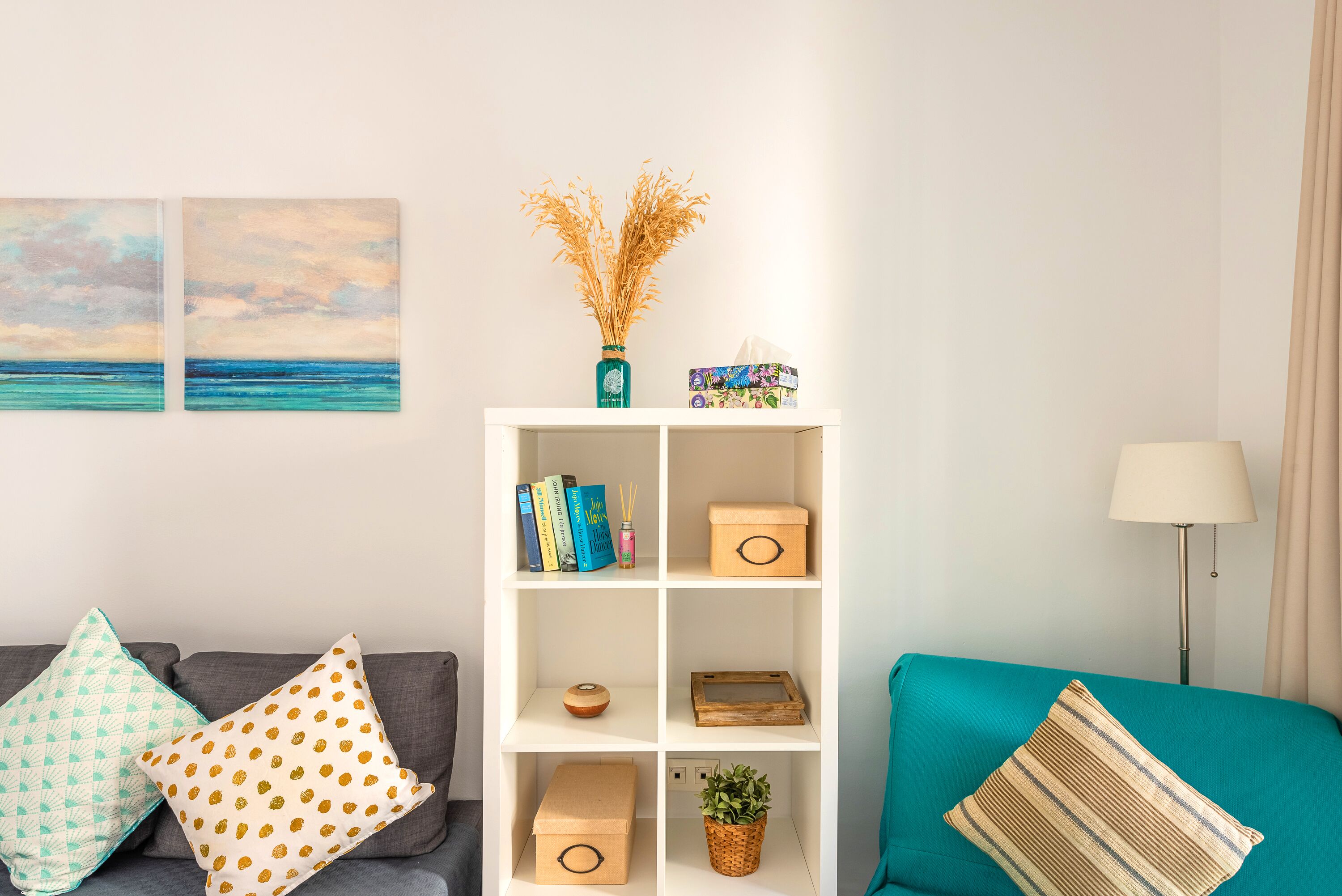 A living room with a sofa, a teal armchair, a white bookshelf, and a lamp.