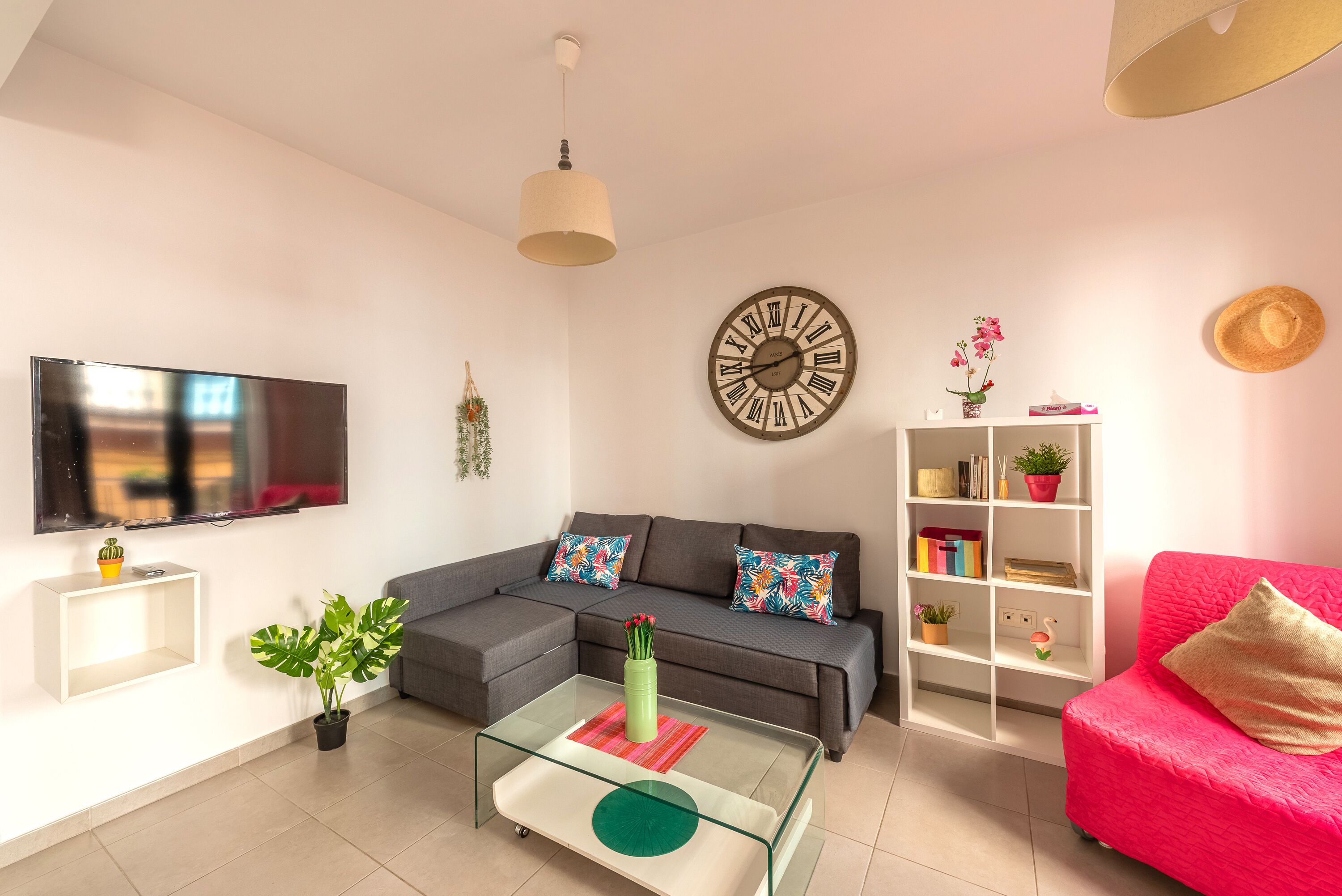 A living room with a sofa, a coffee table, a TV, a bookshelf, and a wall clock.