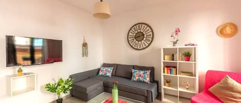 A living room with a sofa, a coffee table, a TV, a bookshelf, and a wall clock.