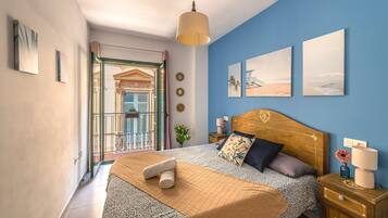 Un dormitorio con cabecera de madera, una cama con colcha estampada, una mesita de noche con lámpara y vistas a un balcón.