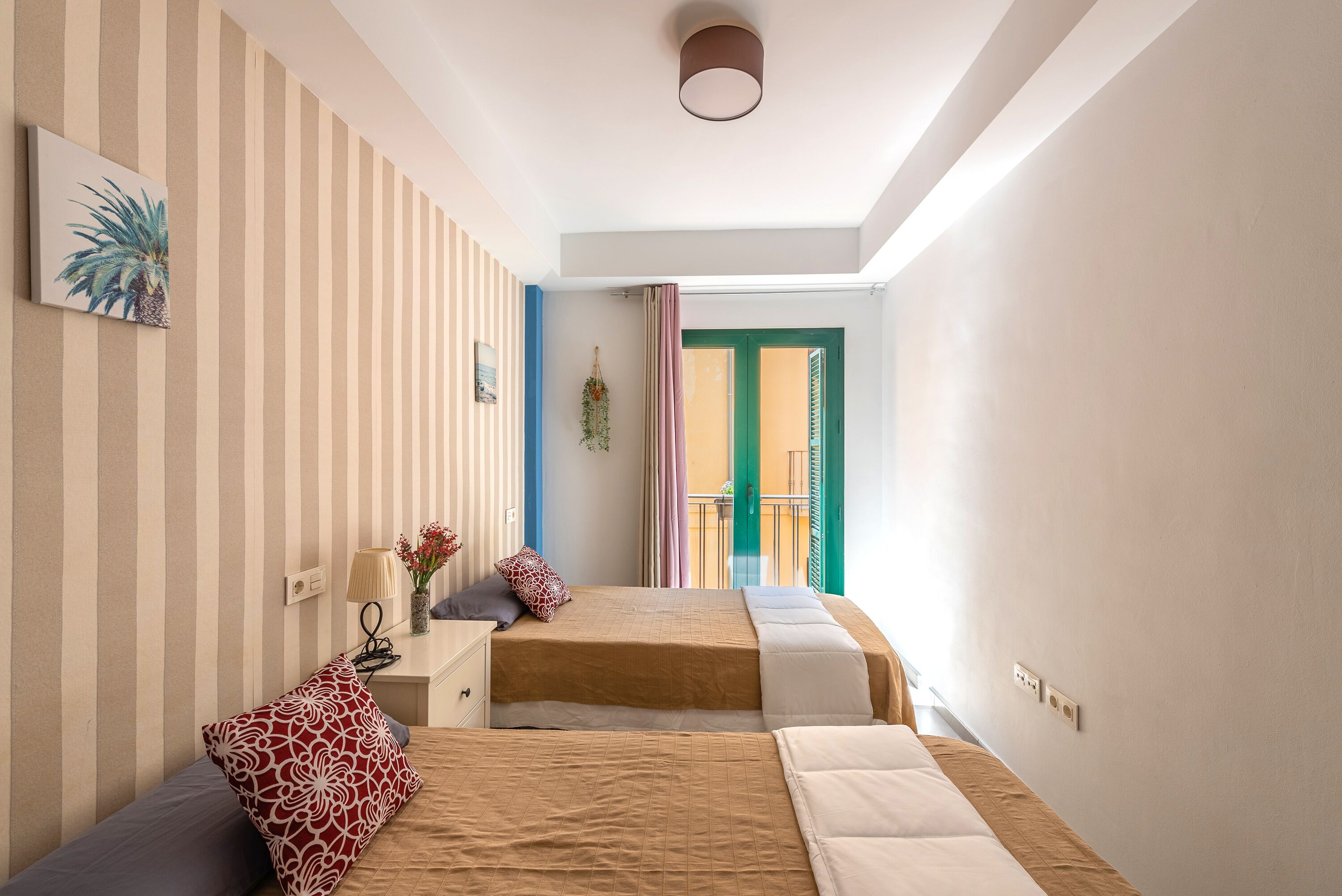 A bedroom with two beds, a striped wall, a small desk, and a window with curtains.