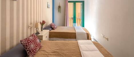 A bedroom with two beds, a striped wall, a small desk, and a window with curtains.