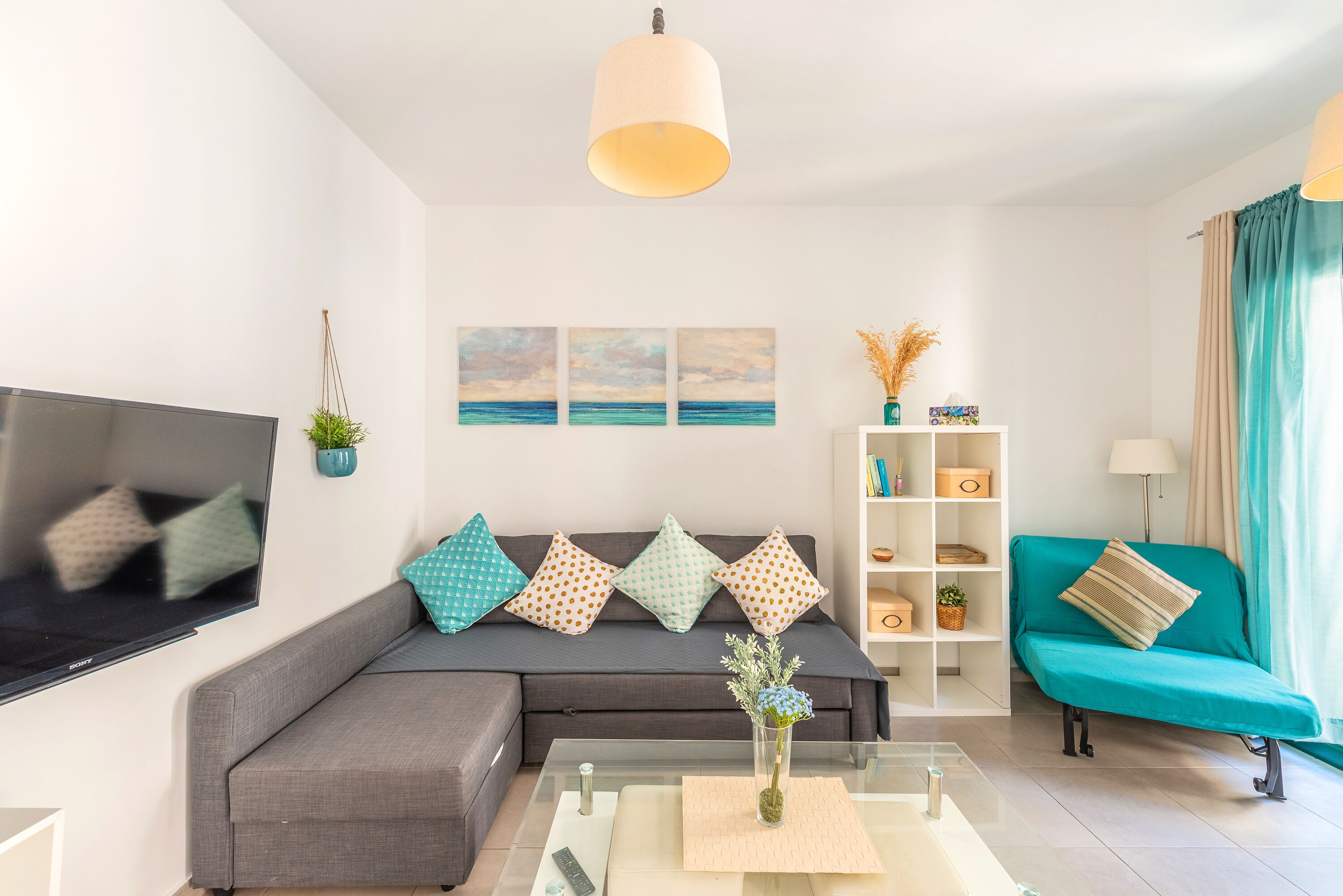 A modern living room with a grey sofa, teal armchair, and a flat-screen TV.