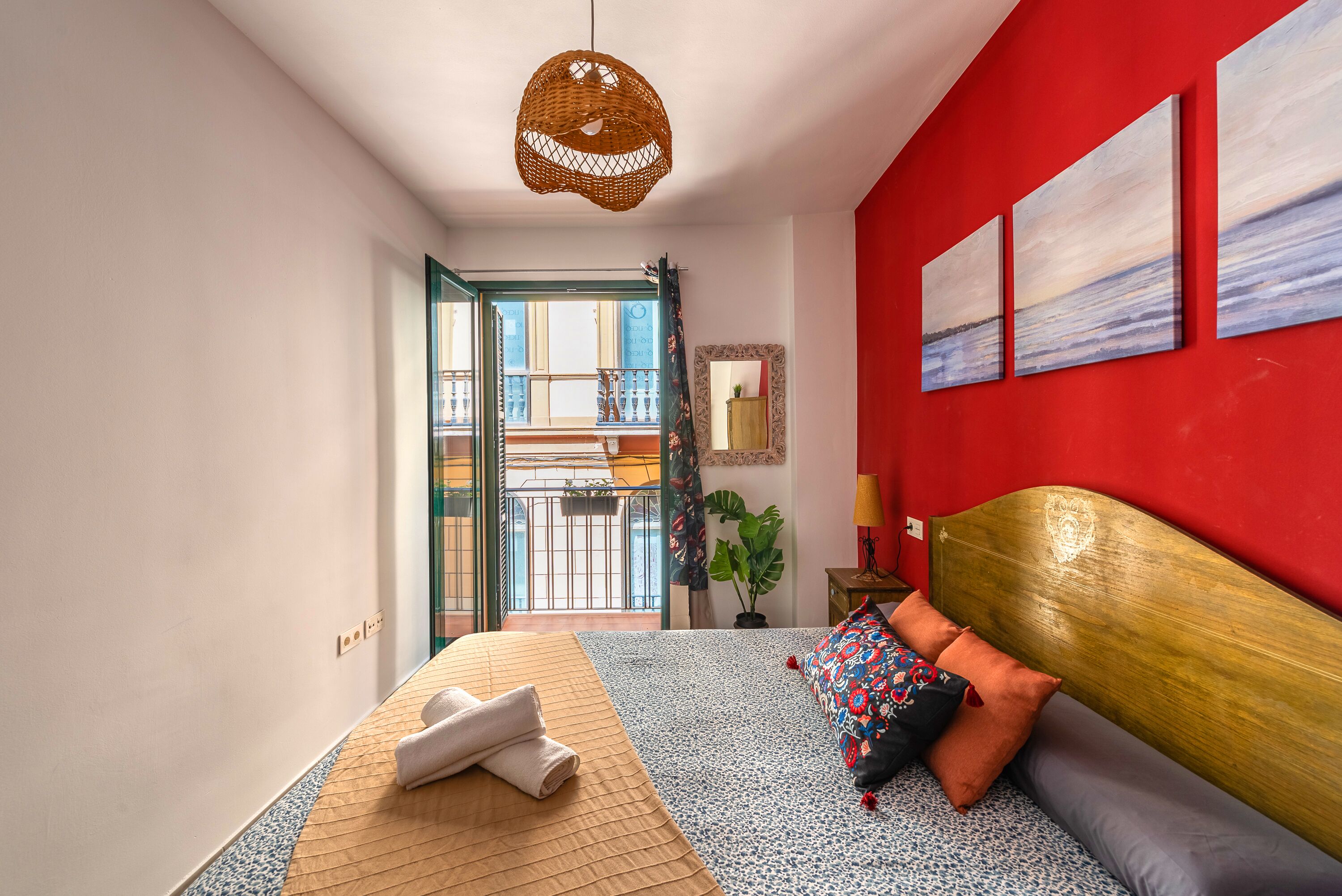 Un dormitorio con cama, pared roja y vista al balcón exterior.