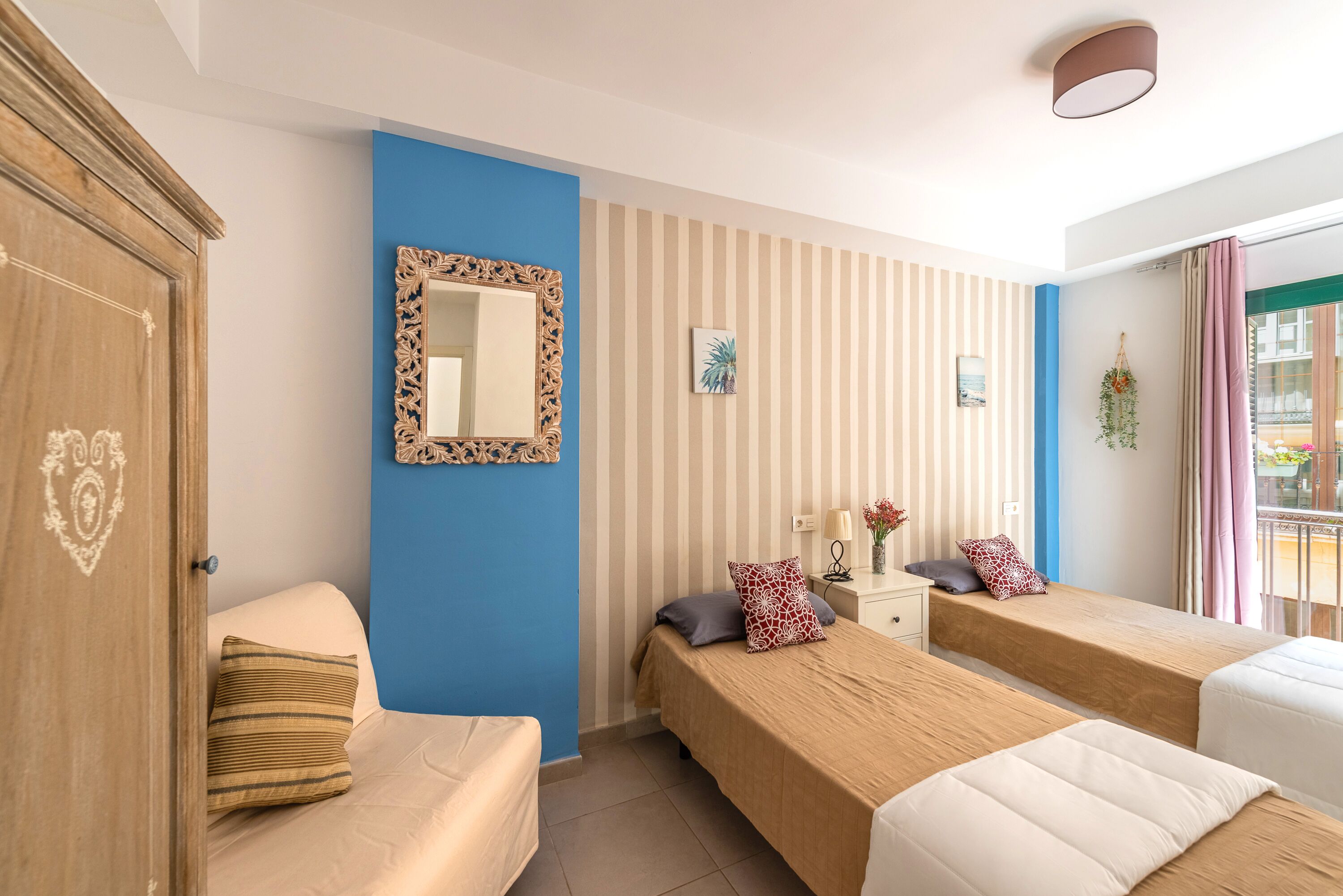 A hotel room with two single beds, a wooden wardrobe, a mirror, and a striped wall.