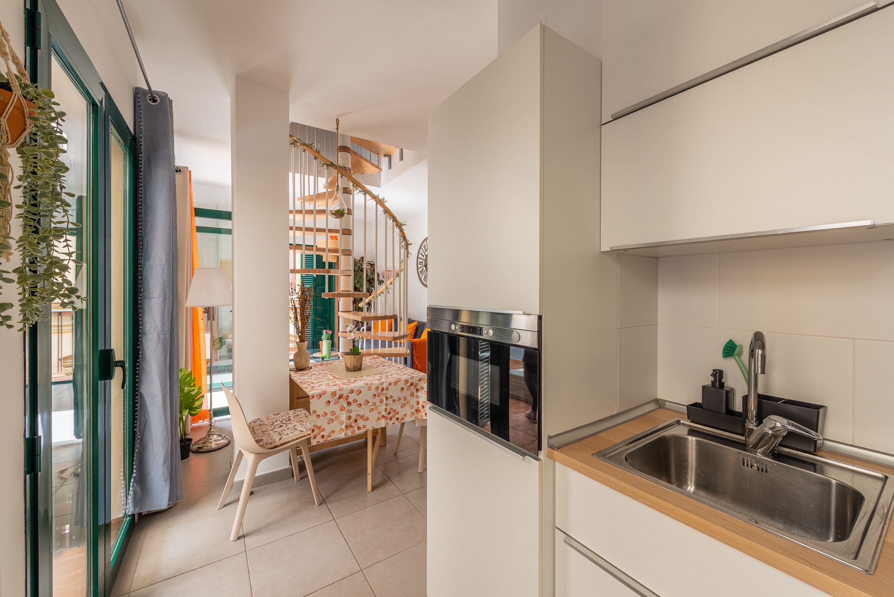 A compact kitchen with a built-in oven, a sink, and a dining area with a table and chairs.