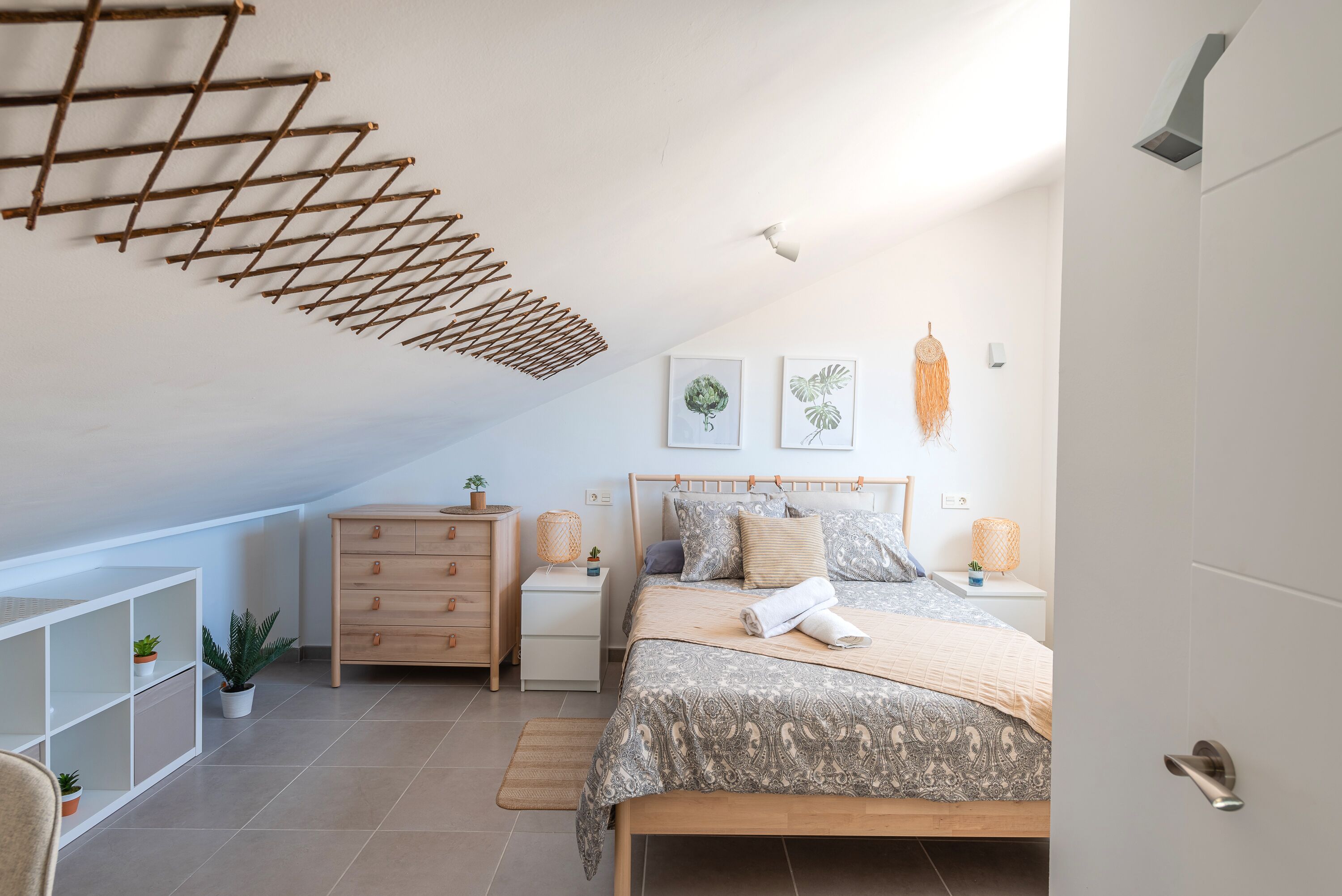 Um quarto com cama, mesas de cabeceira de madeira, cômoda, cabideiro e guarda-roupa branco.