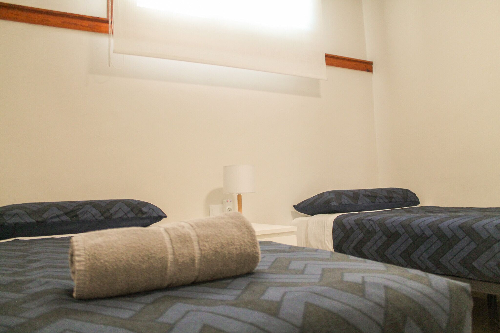 Une chambre d’hôtel avec deux lits, chacun agrémenté de draps et d’oreillers à motifs, une table de chevet avec une lampe et un luminaire fixé au mur.