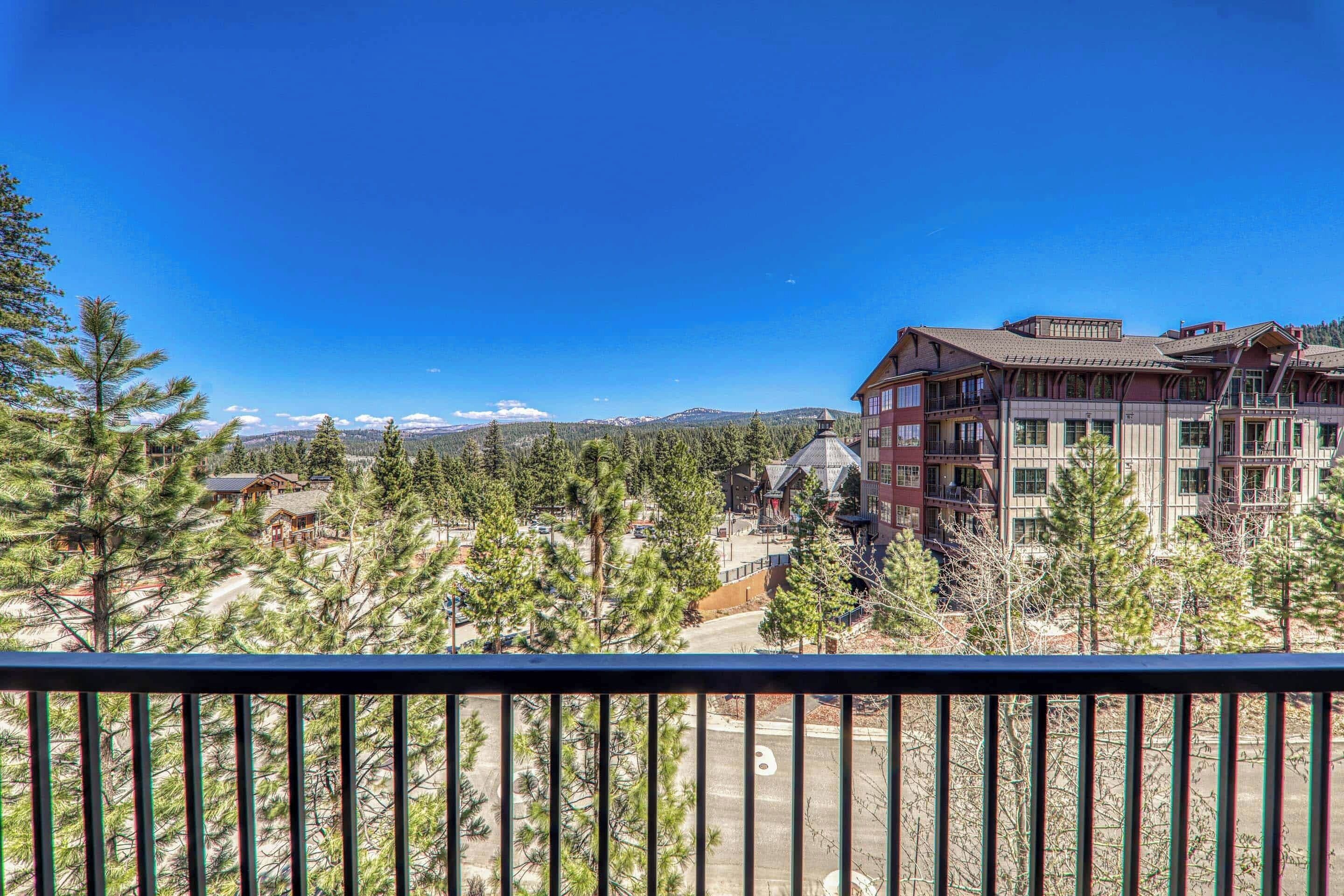 A multi-story building with a traditional architectural style, surrounded by pine trees and a clear blue sky.