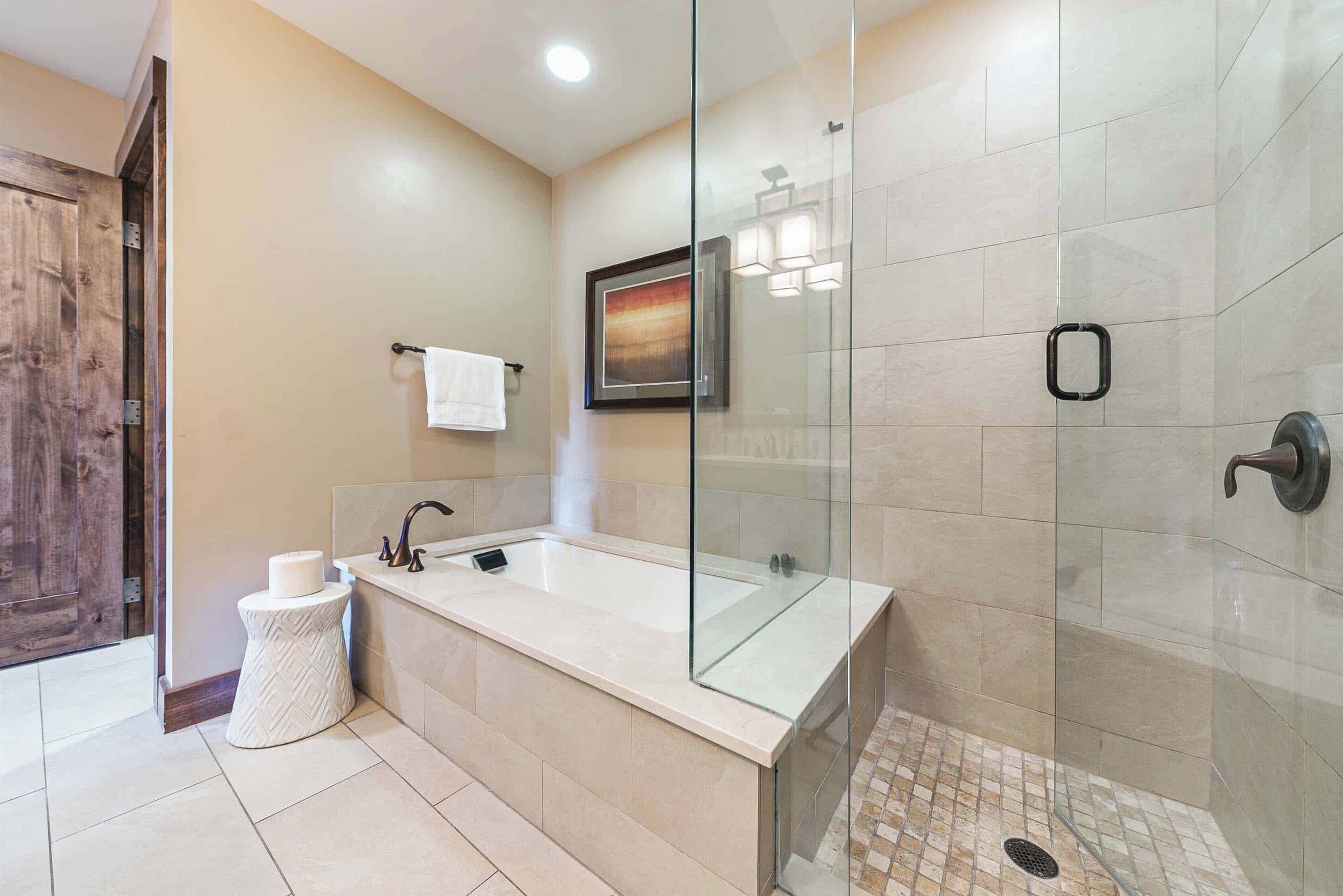 Un baño moderno con ducha de vidrio, una bañera grande y un taburete redondo pequeño.