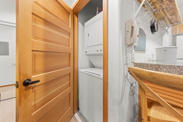 Un área de lavandería con lavadora y secadora, una puerta de madera y un pequeño banco de madera.