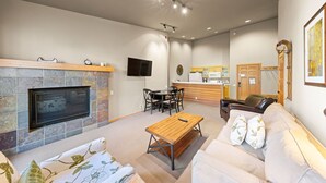Una sala de estar moderna con chimenea, televisor de pantalla plana, zona de comedor y cocina al fondo.