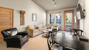 Un salón espacioso con sofá, un sillón de cuero negro, una mesa de comedor con sillas, chimenea y ventanas amplias que ofrecen vistas al exterior.