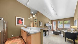 A spacious kitchen with a central island, a dining area with a fireplace, and a living room with a sofa and a TV.