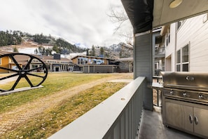 A patio area with a grill, a large outdoor wheel, and a building with multiple windows and a sign. - 716 | Tahoe 2BD Basecamp - Soaks, Swims + W/D (Olympic Valley)