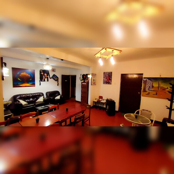 A living room with a red carpet, a black leather sofa, a wooden dining table, and various wall art.