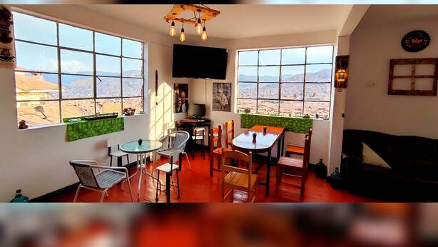 Un vaste espace de vie doté de grandes fenêtres offrant une vue sur le paysage urbain et les montagnes. On y trouve un téléviseur à écran plat fixé au mur, une table en bois avec des chaises et un canapé.