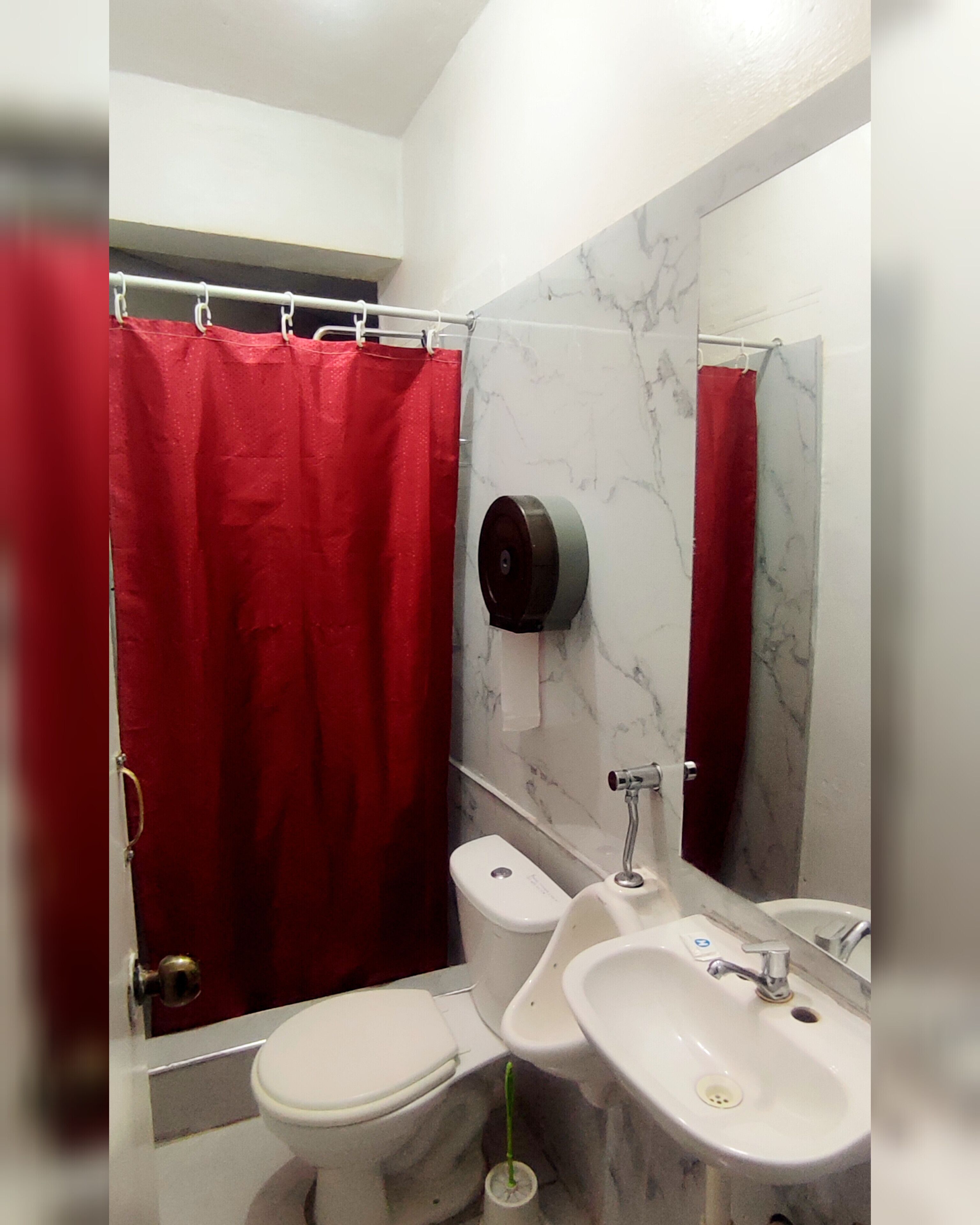 Et badeværelse med et hvidt toilet, en vask og en bruser med rødt gardin.