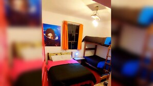 Une chambre de dortoir avec des lits superposés, un bureau, une chaise, une fenêtre avec des rideaux et un luminaire fixé au mur.