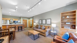 A modern living room with a sofa, coffee table, and a dining area with chairs and a table. There is a kitchen with a microwave and cabinets. - 712 | Outdoor Lover's 2BD - King, Bunks + Pool (Olympic Valley)