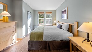 A bedroom with a bed, bedside tables, a dresser, and a window with a view of trees. - 712 | Outdoor Lover's 2BD - King, Bunks + Pool (Olympic Valley)