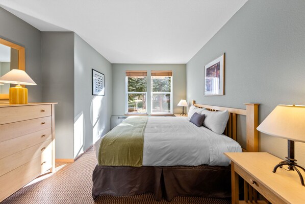 A bedroom with a bed, bedside tables, a dresser, and a window with a view of trees.