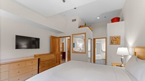 A bedroom with a bed, wooden dresser, TV, and a bathroom visible through an open door. - 521 | Roomy 2BD/2BA - Kitchen, W/D, Pool + Spas (Olympic Valley)
