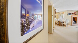 Un couloir orné d’un tableau représentant un paysage enneigé, un coin repas avec une table et des chaises, et une étagère décorative fixée au mur.
