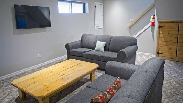 Una sala de estar con un sofá gris, una mesa de centro de madera y un televisor montado en la pared.