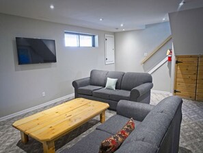 Un salon avec un canapé gris, une table basse en bois et un téléviseur à écran plat fixé au mur.