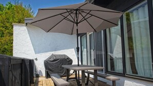 Un patio al aire libre con una mesa, bancos, una sombrilla grande y una parrilla.