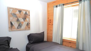 Un dormitorio con dos camas, cabecero de madera, ventana con cortinas y un cuadro decorativo con motivos geométricos.