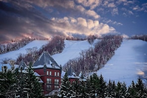 A snow-covered landscape with a red building featuring a steep roof, surrounded by trees and a clear sky.