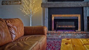 Una sala de estar con un sofá de cuero, una chimenea, un televisor de pantalla plana y un cartel decorativo.