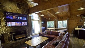 A cozy cabin interior with a stone fireplace, leather sofa, wooden coffee table, and a flat-screen TV displaying Disney content.