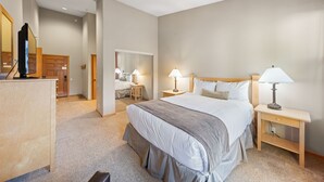 Una habitación de hotel con una cama grande, dos mesitas de noche con lámparas, un aparador de madera y un espejo.