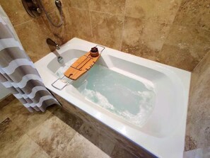 Une baignoire avec un plateau en bois et un petit récipient, une pomme de douche et un porte-serviettes.