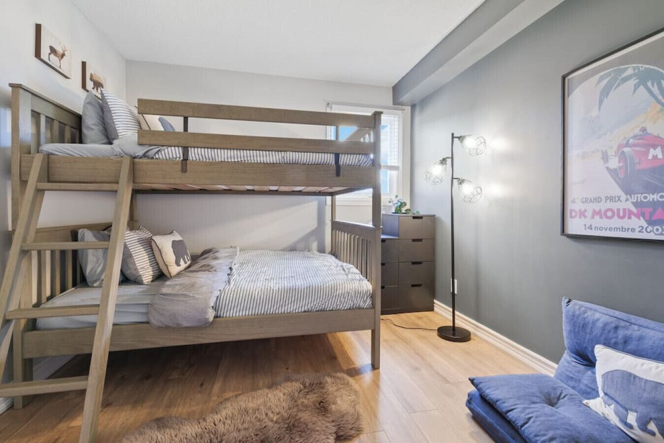 Una cama litera con escritorio y cajones, una lámpara de pie, un cuadro enmarco y un sofá azul.