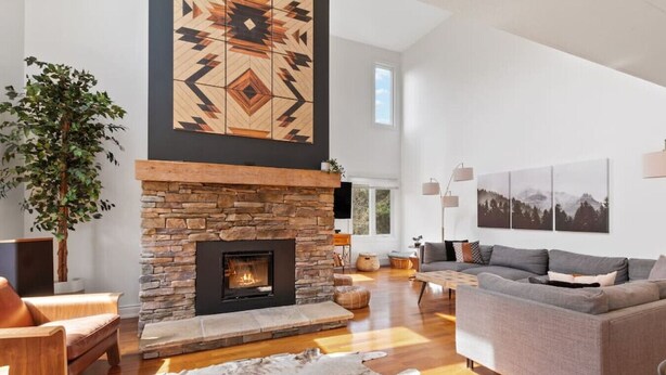 A spacious living room with a stone fireplace, a large plant, and a grey sofa. - Modern/Rustic 2 Story Condo/3 Min Walk to Village (The Blue Mountains)