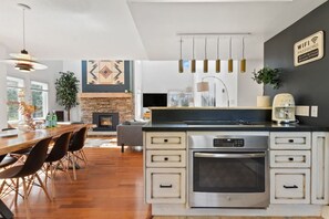 A modern kitchen with a central island, built-in oven, and a dining area with a wooden table and chairs.