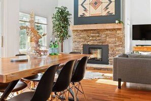 A modern living room with a stone fireplace, a dining area with a wooden table and black chairs, and a grey sofa.