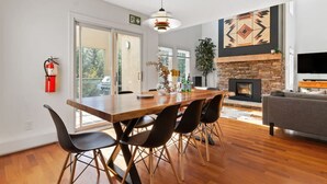 A modern living room with a fireplace, a dining area with a wooden table and chairs, and a large window offering a view of the outdoors. - Modern/Rustic 2 Story Condo/3 Min Walk to Village (The Blue Mountains)