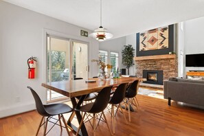 Un salon moderne avec une cheminée, un coin repas avec une table et des chaises en bois, et une grande fenêtre donnant sur l’extérieur.