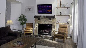 A living room with a stone fireplace, two armchairs, a sofa, a television, and a plant.