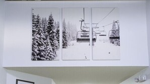 A hallway with framed certificates on the left, a sofa and lamp in the center, and a ski-themed poster on the right.