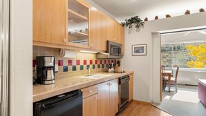 A compact kitchen with wooden cabinets, a stainless steel coffee maker, a microwave, and a dishwasher. - 253 | Studio w/ Mtn Views & A/C! Stay n Play! (Olympic Valley)