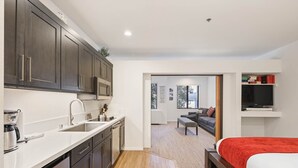 A compact hotel room with a kitchenette, a bed with a red blanket, a TV, and a seating area with a sofa and a small table. - 252 | Chic Summer Studio - Pool + Tubs Await (Olympic Valley)